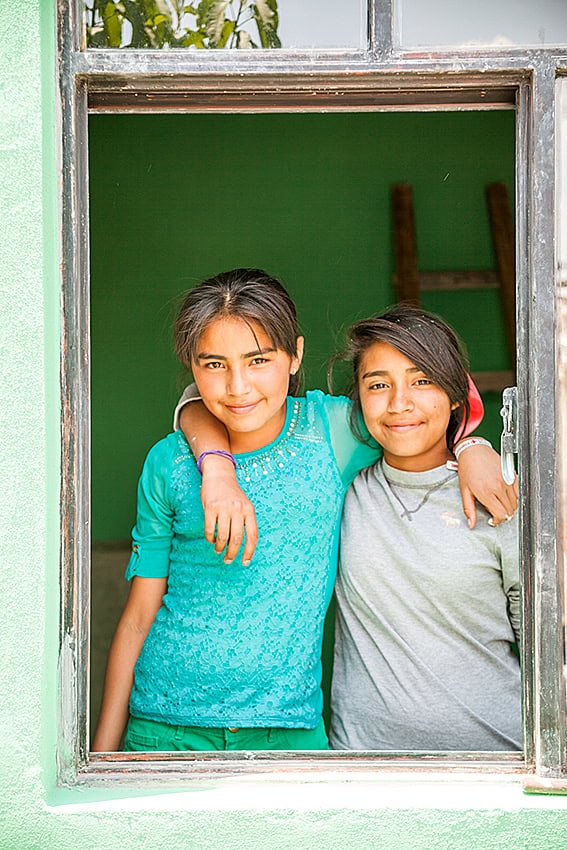 Smiling schoolgirls embracing at an open window in San Miguel, emphasizing education and community.